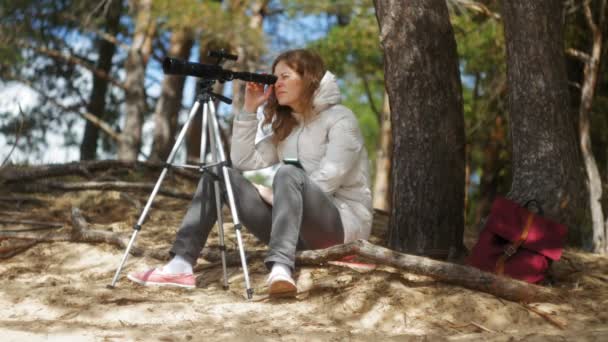 Aantrekkelijke vrouw kijkt door een telescoop in een forest op de rivieroever — Stockvideo