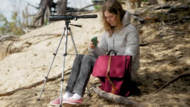 Привлекательная женщина смотрит в телескоп в лесу на берегу реки — стоковое видео