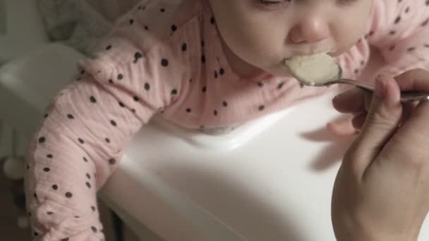 Mamá alimenta a una niña en una silla alta . — Vídeos de Stock