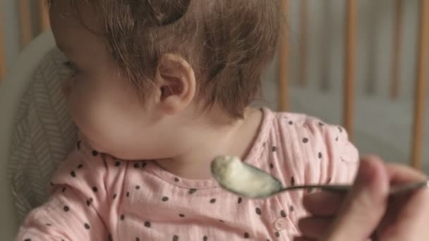 Moeder voedt een klein meisje in een kinderstoel. — Stockvideo