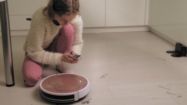 Een jonge vrouw stofzuigt een robot. — Stockvideo