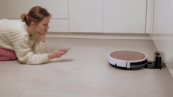 Een jonge vrouw bestuurt een robot met een stofzuiger. — Stockvideo