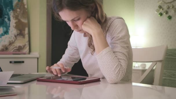 Una mujer joven trabaja en una tableta de computadora en casa . — Vídeo de stock