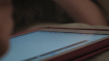 Küçük çocuklar, erkek ve kız kardeşler yatmadan önce yatağa uzanıp tablet üzerinde oynuyorlar..