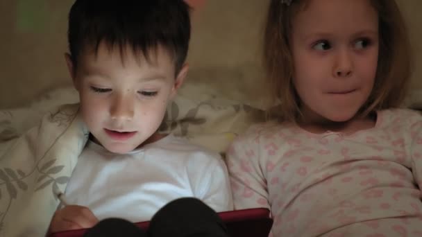 어린아이들, 친형제 자매들 이 침대에 누워 있고 잠자리에 들기 전에 타블렛에서 놀고 있다. — 비디오