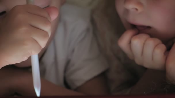 I bambini piccoli, fratello e sorella sono sdraiati sul letto e giocano sul tablet prima di andare a letto . — Video Stock