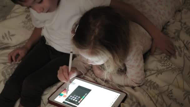 Petits enfants, frère et sœur sont allongés sur le lit et jouent sur la tablette avant d'aller au lit . — Video