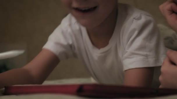 Los niños pequeños, el hermano y la hermana están acostados en la cama y jugando en la tableta antes de irse a la cama . — Vídeo de stock