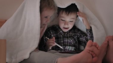 Çocuklar yatakta yatarken bir tablet kullanır.