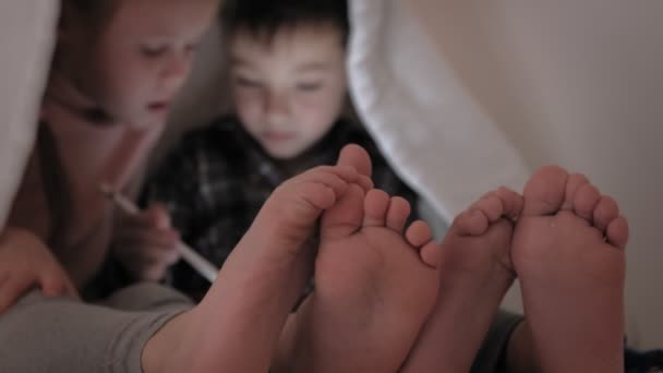 As crianças usam um tablet enquanto estão deitadas na cama — Vídeo de Stock