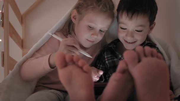 Děti při ležení v posteli užívají tabletu — Stock video