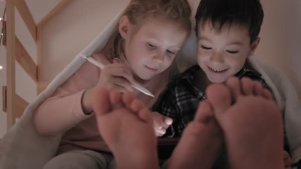 Kinderen gebruiken een tablet terwijl ze in bed liggen — Stockvideo