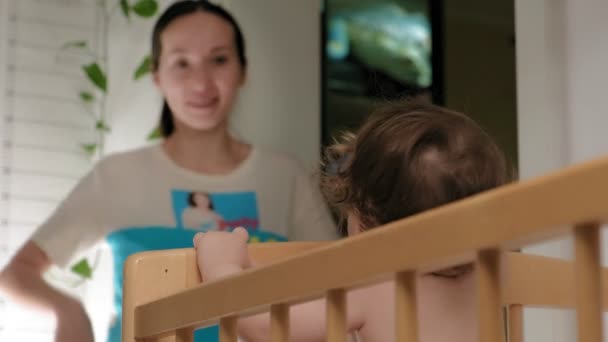 Woman playing with a baby beginner standing in a crib — Stock Video