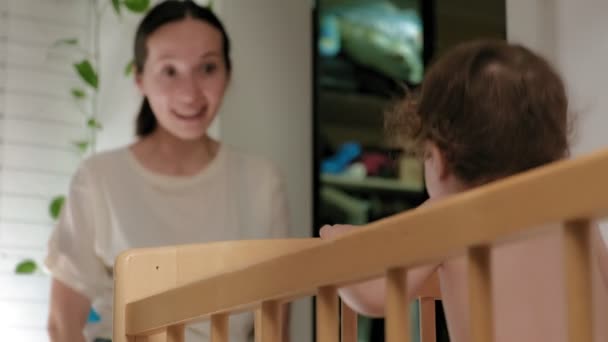 Woman playing with a baby beginner standing in a crib — Stock Video