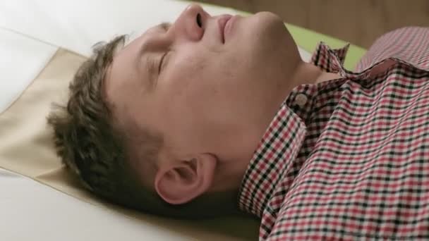 Mężczyzna leży na łóżku do masażu z jadeitowymi rolkami. — Wideo stockowe