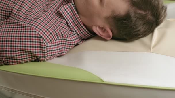Bir adam masaj yatağında yeşil bigudilerle yatıyor.. — Stok video