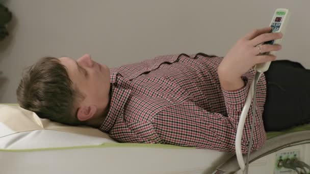Ένας άντρας ξαπλώνει σε ένα κρεβάτι μασάζ με ρολά νεφρίτη.. — Αρχείο Βίντεο