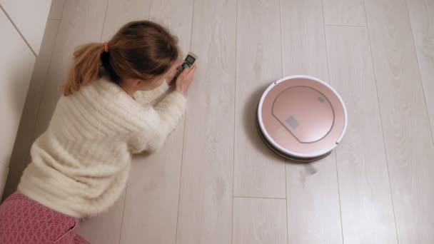Genç bir kadın elektrikli süpürgeyle robotu kontrol ediyor.. — Stok video