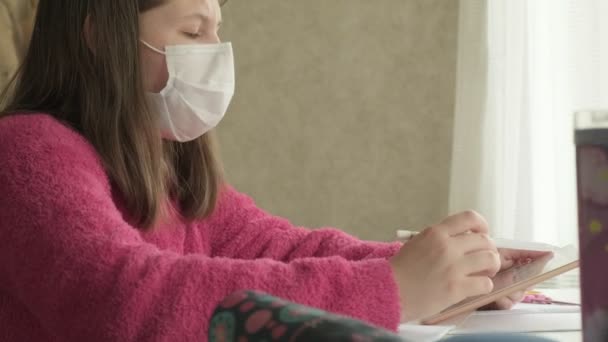 コロナウイルスのパンデミックの間に家で勉強している医療マスクの女の子 — ストック動画