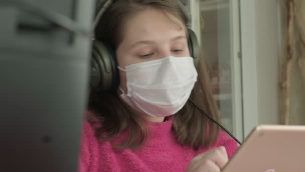 Девочка в медицинской маске учится дома во время пандемии коронавируса — стоковое видео