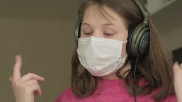 Девочка в медицинской маске учится дома во время пандемии коронавируса — стоковое видео