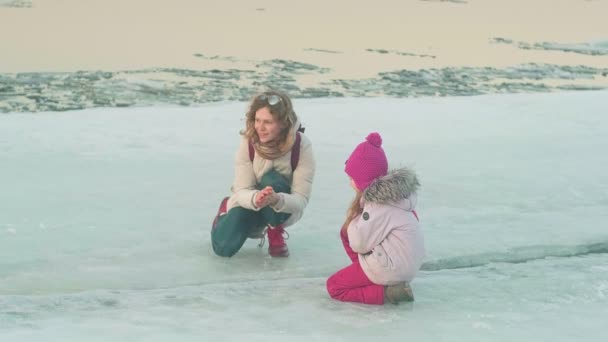 Женщина с ребенком гуляет по замерзшей реке весной на закате . — стоковое видео