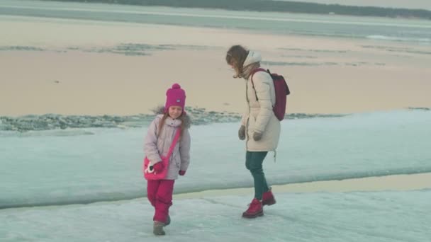 Una donna con un bambino cammina su un fiume ghiacciato in primavera al tramonto . — Video Stock