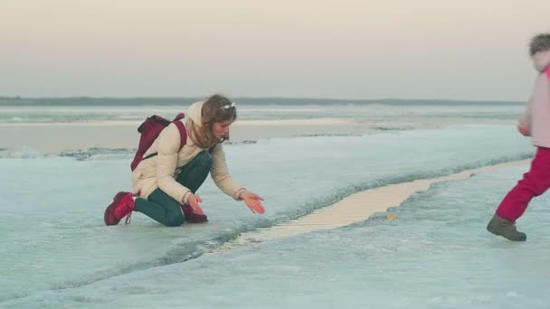 Μια γυναίκα με παιδί περπατάει σε παγωμένο ποτάμι την άνοιξη το ηλιοβασίλεμα.. — Αρχείο Βίντεο