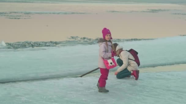 Une femme avec un enfant marche sur une rivière gelée au printemps au coucher du soleil . — Video