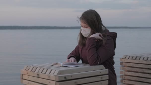 Een jong meisje met een zwart masker alleen buiten. Coronaviruspandemie — Stockvideo