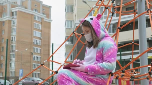 Menina em uma máscara protetora no parque infantil . — Vídeo de Stock