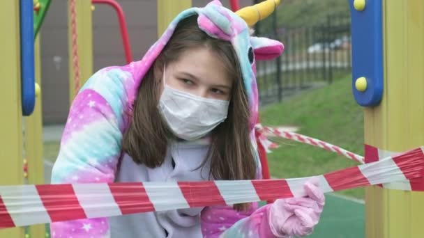 Menina em uma máscara protetora no parque infantil . — Vídeo de Stock