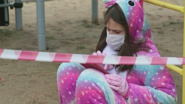 Menina em uma máscara protetora no parque infantil . — Vídeo de Stock