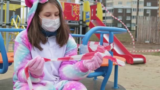 Menina em uma máscara protetora no parque infantil . — Vídeo de Stock