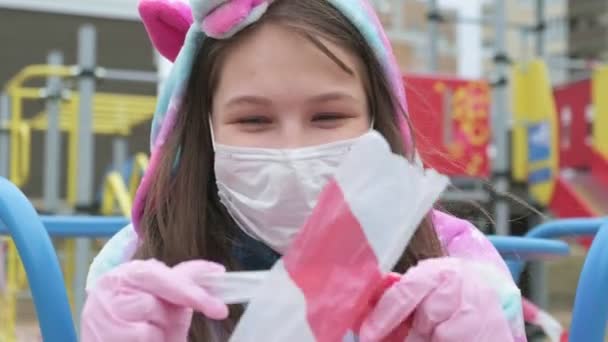 Menina em uma máscara protetora no parque infantil . — Vídeo de Stock