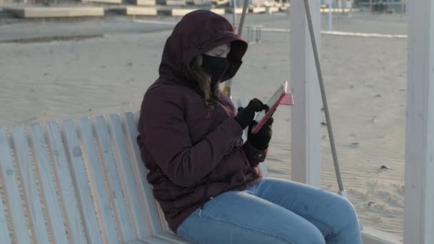 Дівчина в масці на відкритому повітрі використовує планшет. ізоляція — стокове відео