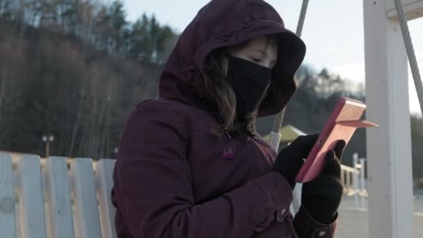 Girl in a mask outdoors uses a tablet. insulation — Stock Video