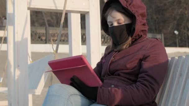 Дівчина в масці на відкритому повітрі використовує планшет. ізоляція — стокове відео