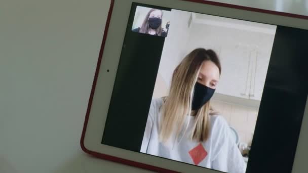 Dos mujeres jóvenes están hablando a través de enlace de vídeo en máscaras médicas — Vídeo de stock