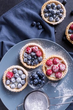 Büyük gri bir tabakta taze yaban mersini ve ahududu ile lezzetli bir tatlı. Siyah arka plan. en üstteki görünüm
