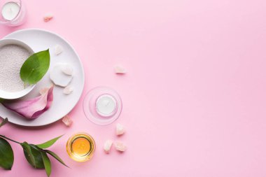 Yağlı spa kompozisyonu, deniz tuzu, mumlar ve pastel pembe arka planda tropikal bitkiler. Üst görünüm, boşluk kopyala