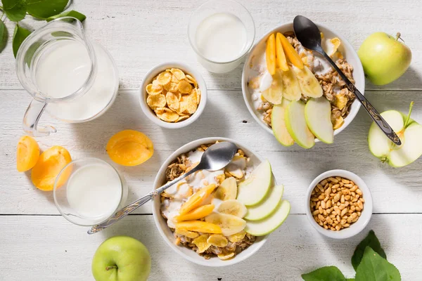 Granola, meyve, yoğurt ve beyaz ahşap arka planda sütle dolu iki bardak. Sağlıklı kahvaltı gevreği üst görünümü
