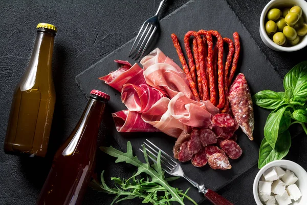 Tapas konsepti. Prosciutto, sosisli sucuk, şişe bira, zeytin, roka, fesleğen ve peynir. Antipasti konsepti. Üst görünüm.
