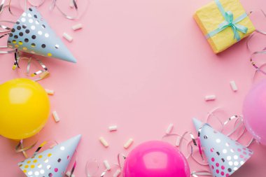 Doğum günü şapkaları, pembe, sarı toplar, sarı hediye kutusu ve pembe arka planda gümüş yılan yağı. Tatil geçmişi. Boşluğu kopyala, üst görünüm