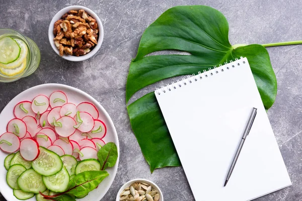 Salatalıklı hafif turp salatası, arınma içeceği limonlu, cevizli ve balkabağı tohumlu gri arka planda. Sağlıklı beslenme konsepti. Üst görünüm, alanı kopyala