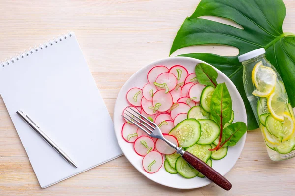 Salatalıklı hafif turp salatası ve büyük bir canavar yaprağının arka planında salatalıklı ve limonlu detoks suyu. Sağlıklı beslenme, Keto diyeti. Üst görünüm, alanı kopyala