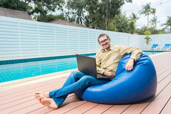 Mann mit Brille arbeitet am Laptop, während er auf dem Sitzsack sitzt — Stockfoto