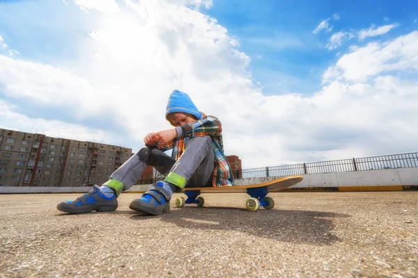 Jongen op straat zitten op skateboard — Stockfoto