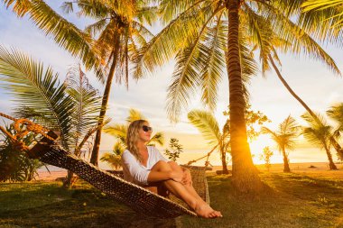 Sahilde hamakta oturmuş ve günbatımı zevk mutlu kadın. 