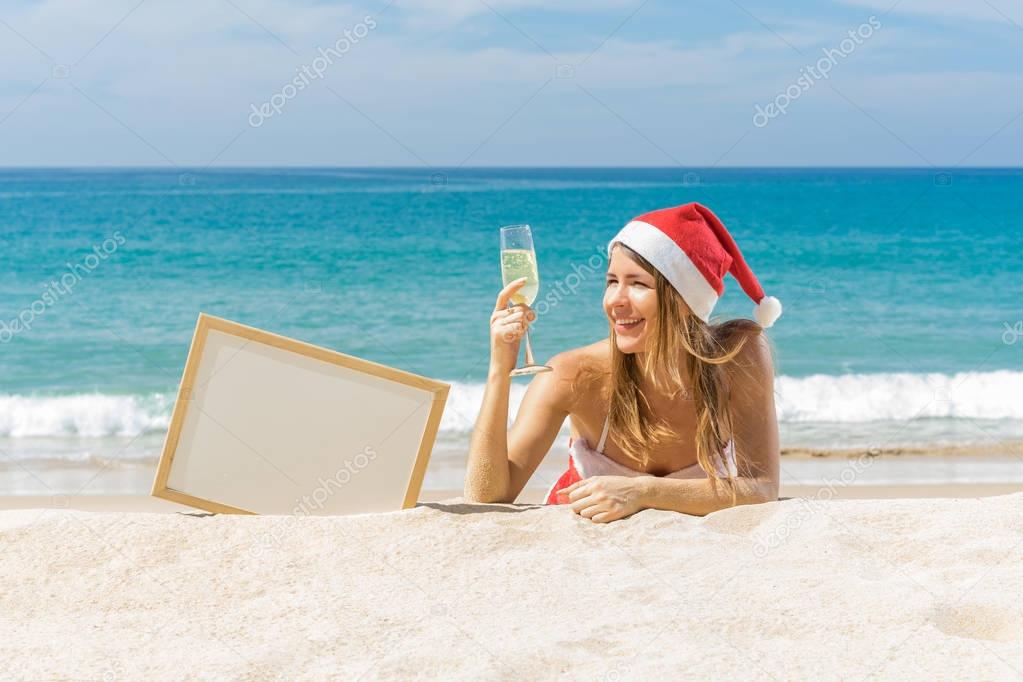 Santa girl on the beach with white board for write your text. Tropical vacation. Christmas and new year concept